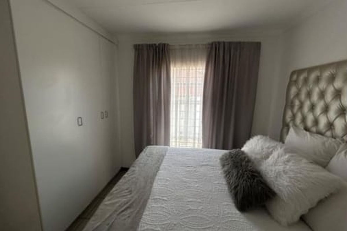 A bedroom featuring built-in floor-to-ceiling wardrobes and a window with curtains.