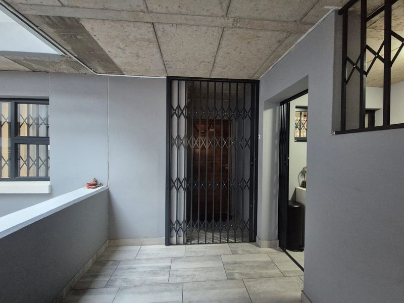 A secure entrance area featuring tiled flooring, an exposed concrete ceiling, and a metal security gate protecting the main doorway.
