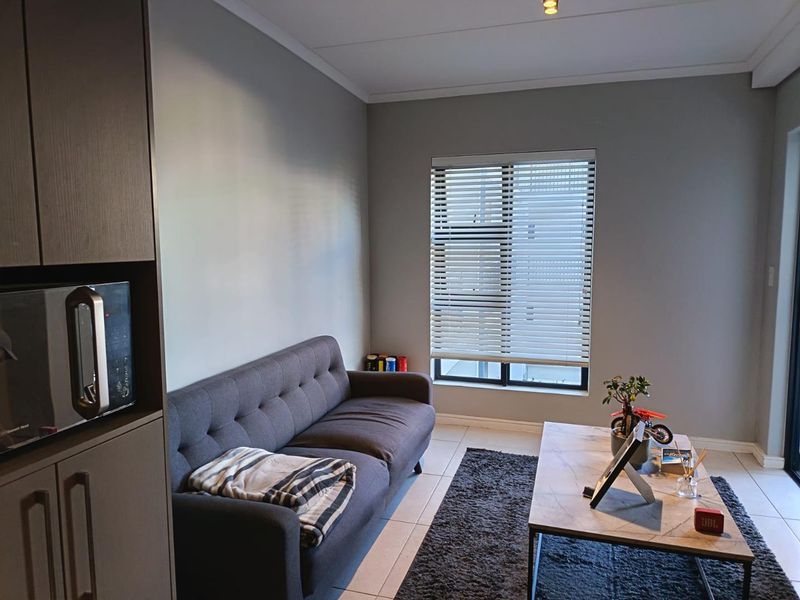 A modern living room featuring neutral grey walls, tiled flooring, built-in cabinetry, and a window fitted with venetian blinds.