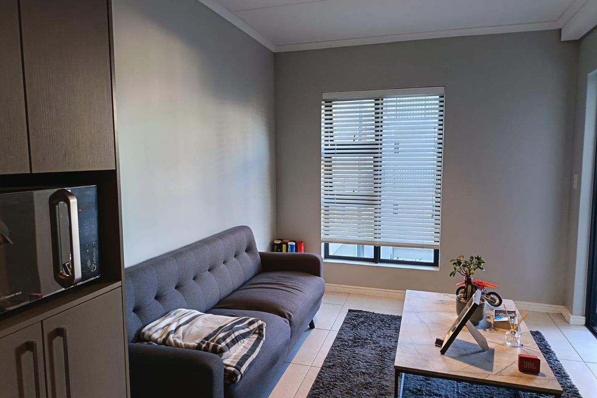 A modern living room featuring neutral grey walls, tiled flooring, built-in cabinetry, and a window fitted with venetian blinds.