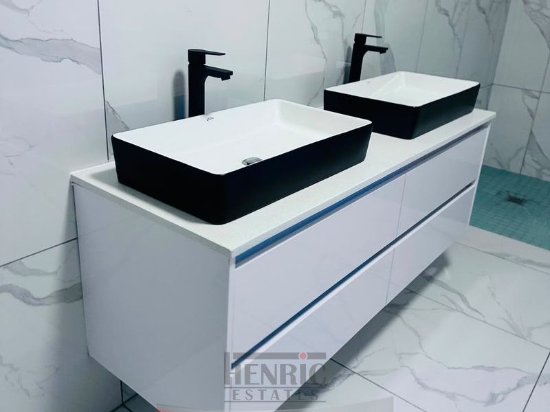 Modern bathroom featuring a sleek double vanity with vessel sinks, matte black faucets, and contemporary marble-look wall and floor tiling.