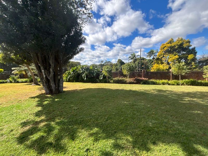 A well-maintained, spacious private garden featuring a lush green lawn, mature trees, and a secure brick boundary wall.