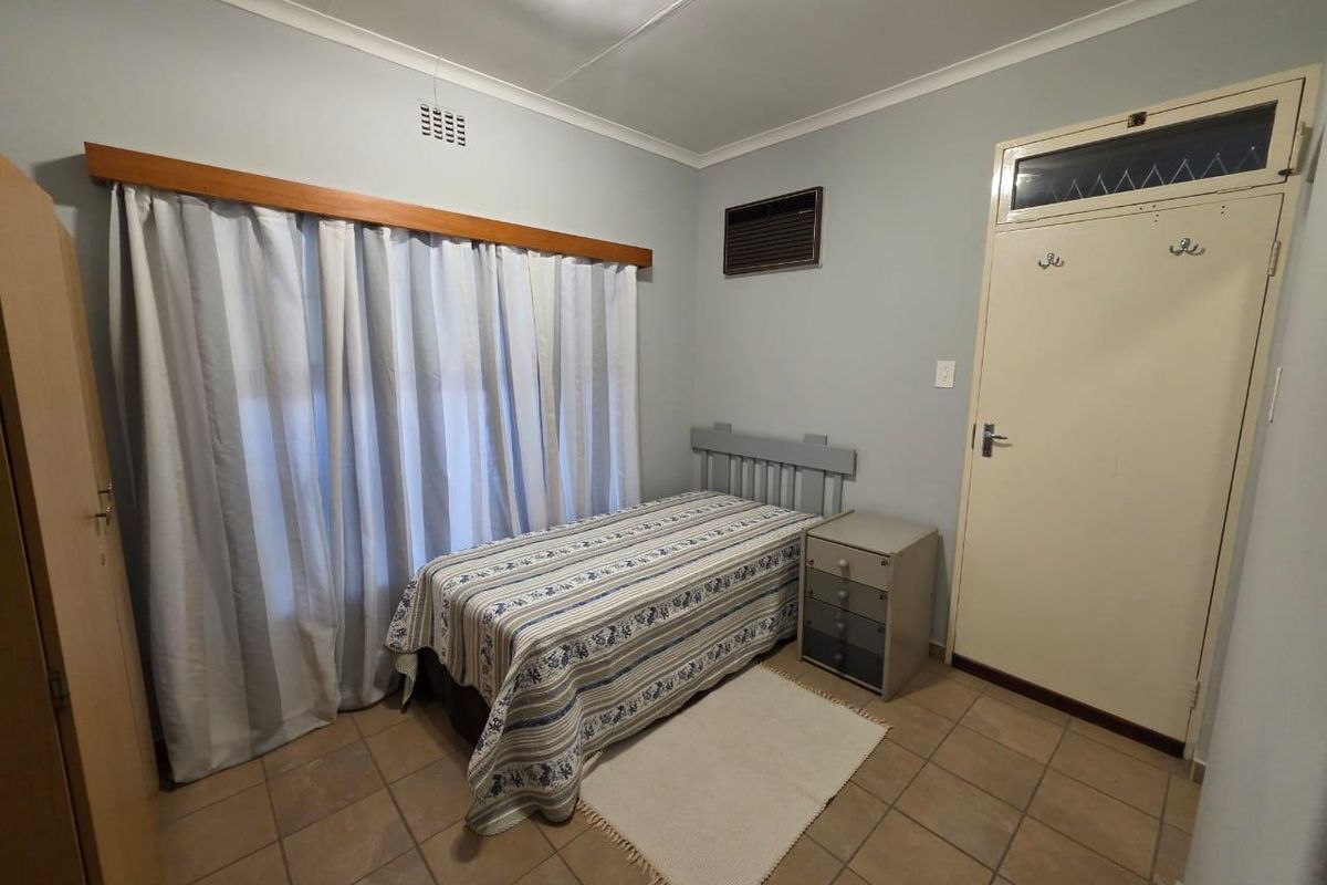 A functional bedroom featuring tiled flooring, a built-in air conditioning unit, and a classic door with a transom window.