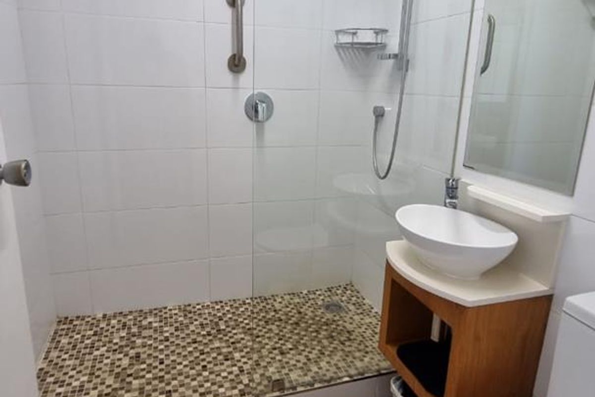 Modern bathroom featuring a walk-in shower with glass screen, mosaic tile flooring, vanity basin, and wood-look flooring.