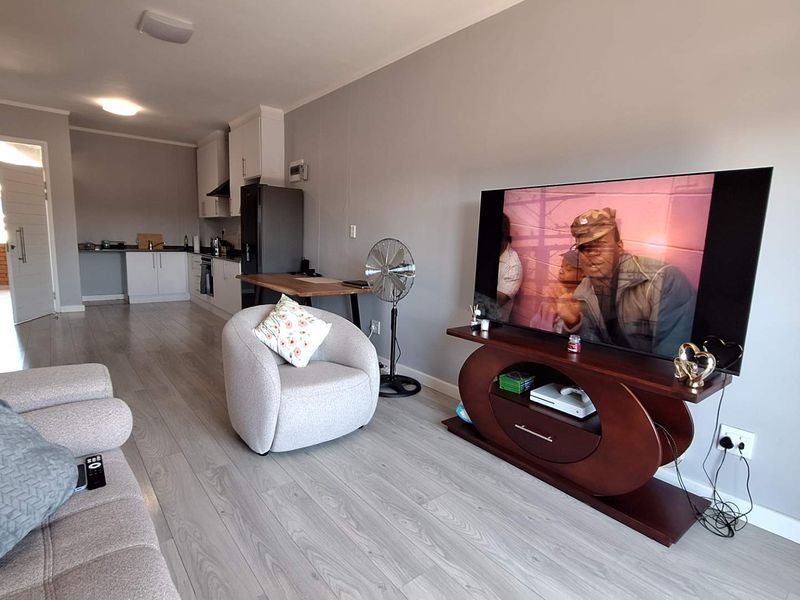 An open-plan living area featuring light-toned laminate flooring and a modern kitchen with built-in cabinetry, oven, and extractor fan.