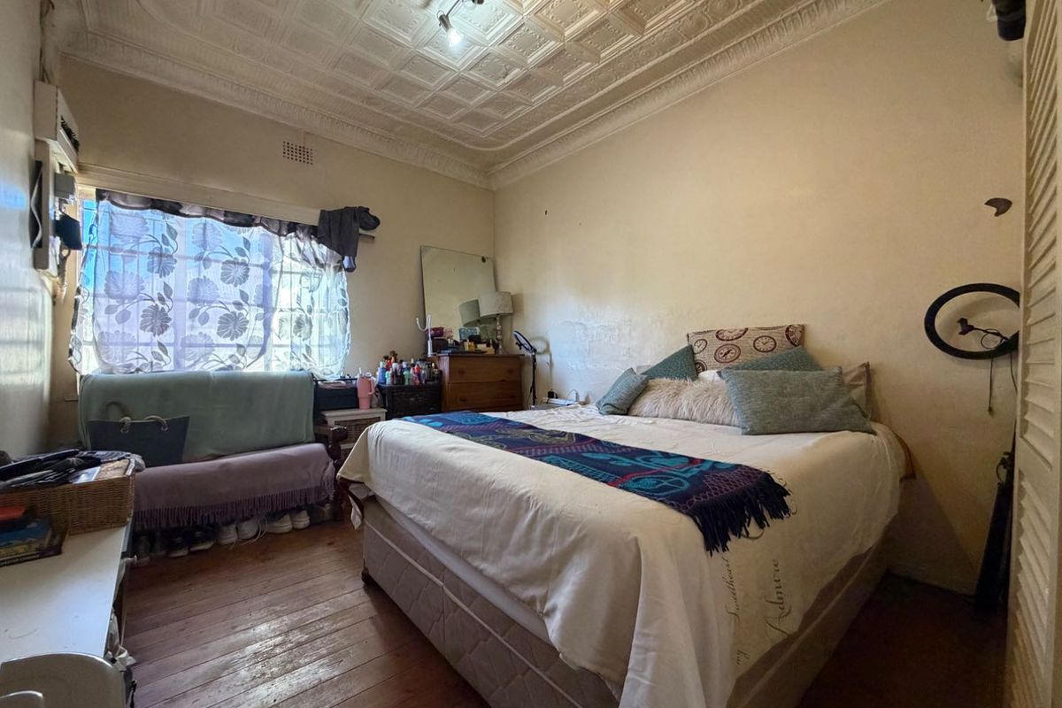 A bedroom featuring original pressed metal ceilings and timber flooring, offering a classic architectural character in need of cosmetic refurbishment.