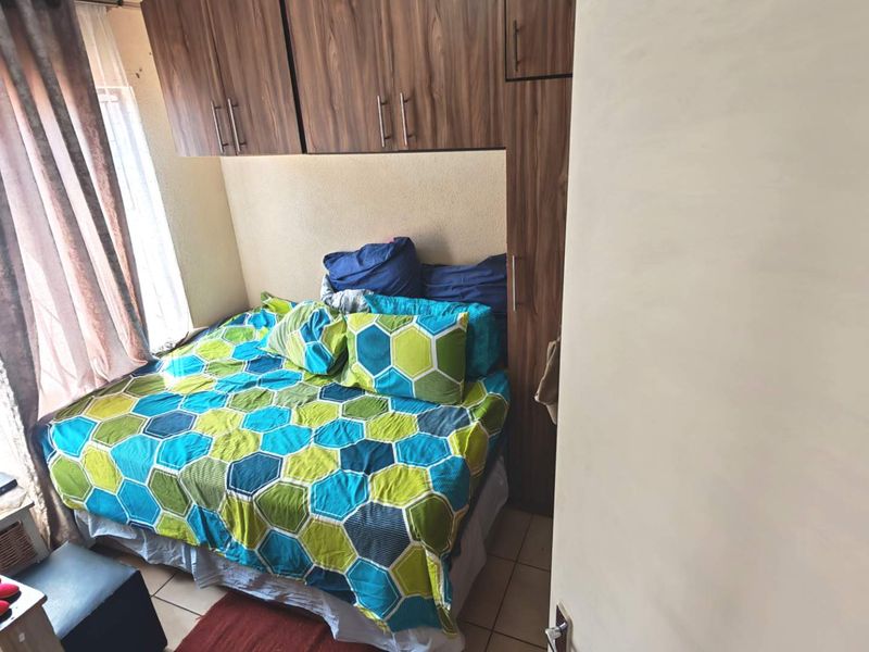 A compact bedroom featuring built-in wooden cupboards and tiled flooring, providing functional storage space.