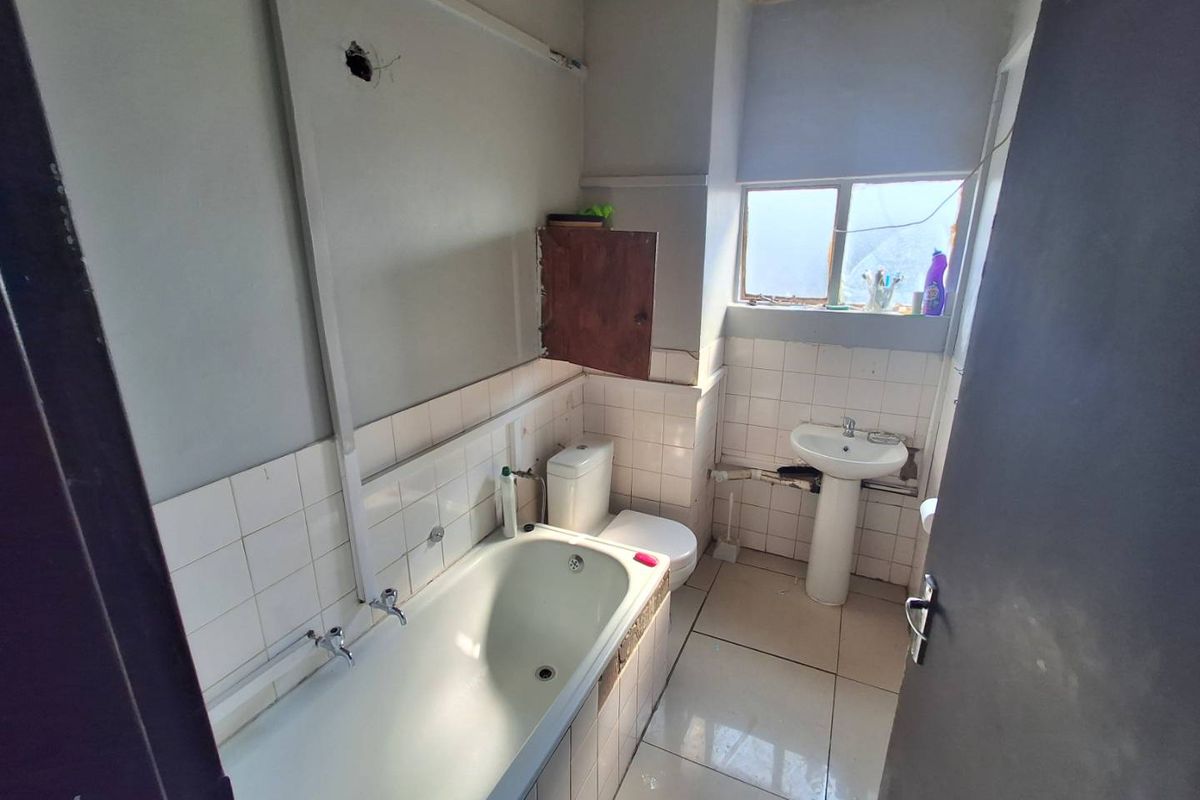 A dated bathroom featuring a bathtub, pedestal basin, and toilet, requiring renovation and cosmetic repairs to the walls and fixtures.
