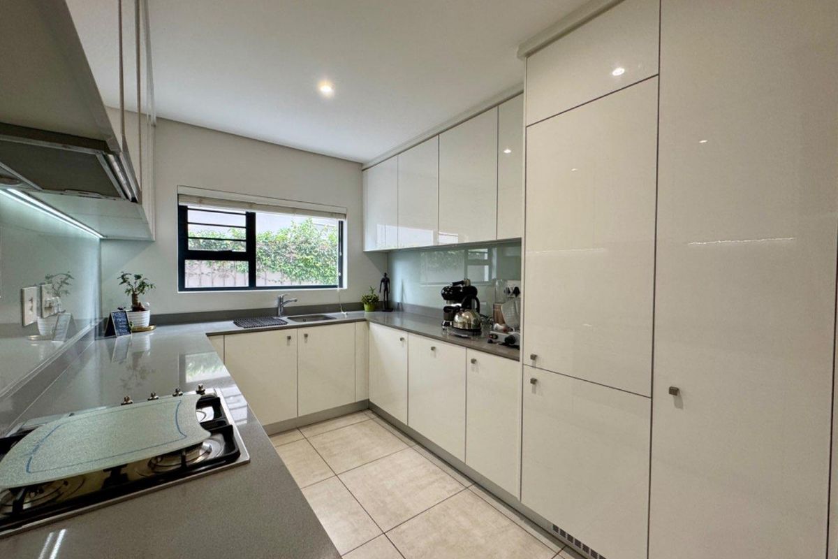 Modern kitchen featuring sleek white cabinetry, stone countertops, integrated appliances, and tiled flooring with ample natural light.