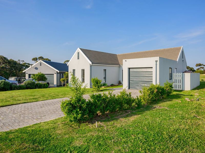 Front view of a modern single-story house featuring a tiled roof, paved driveway, and an integrated garage, set within a well-maintained garden.
