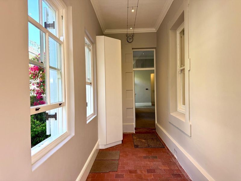 A bright, well-maintained hallway featuring terracotta tile flooring, classic sash windows, and built-in corner cabinetry, leading into the interior living spaces.