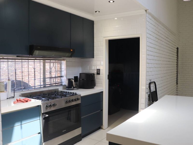 Modern kitchen featuring dark blue cabinetry, stone countertops, subway tile backsplash, and a gas stove, with an adjacent scullery area.