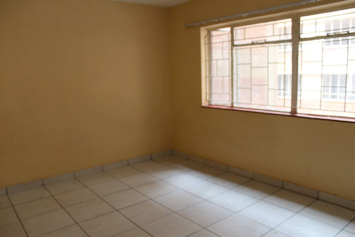 A vacant bedroom featuring tiled flooring and a window fitted with security bars.
