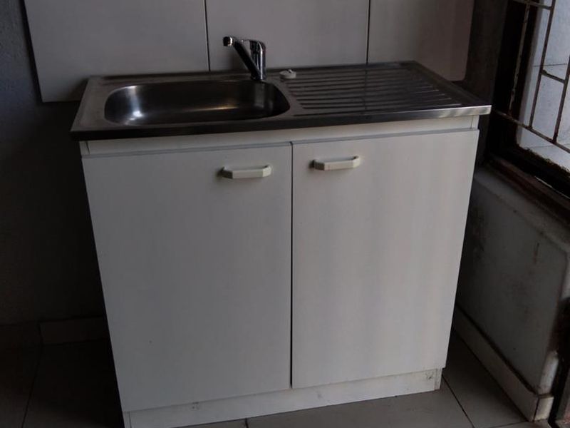 A basic scullery or utility area featuring a stainless steel sink, built-in base cabinetry, and tiled splashback.