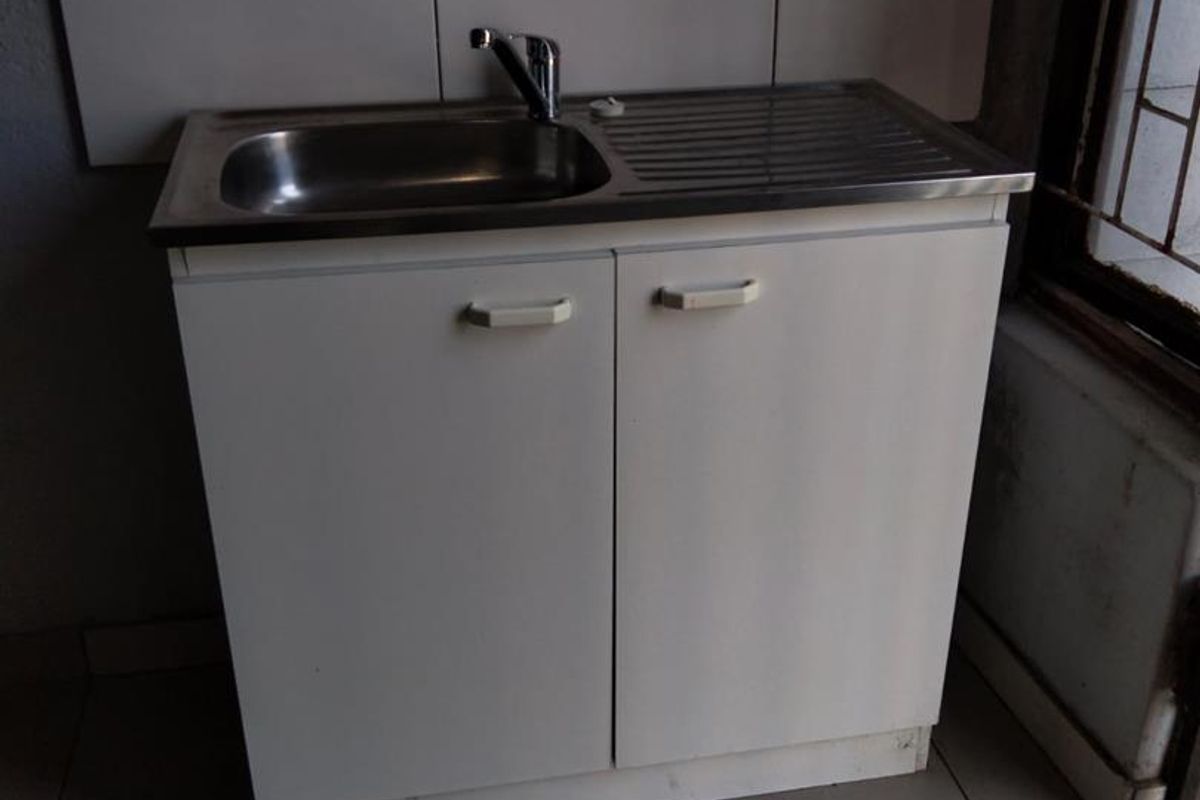 A basic scullery or utility area featuring a stainless steel sink, built-in base cabinetry, and tiled splashback.