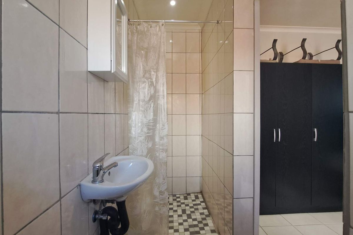 A functional bathroom featuring a wall-mounted basin, a shower area with a curtain, and tiled finishes, adjacent to a built-in storage cupboard.