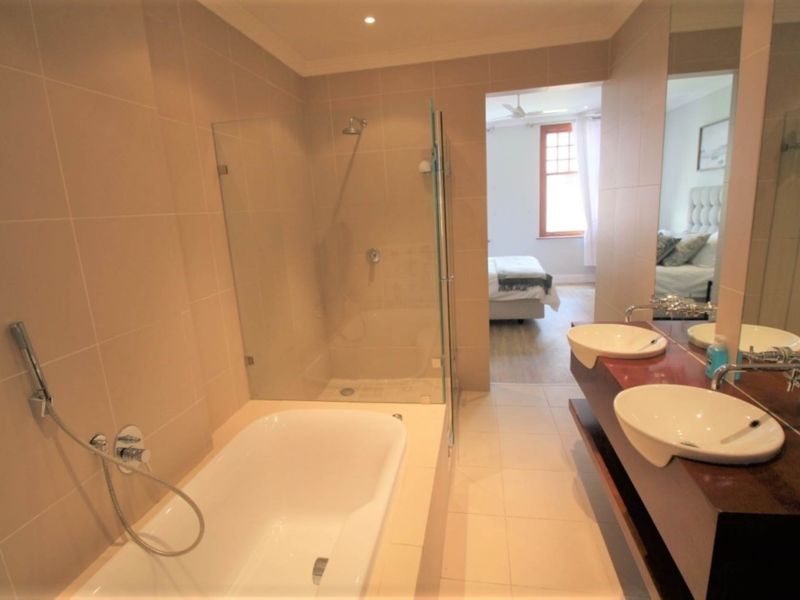Modern bathroom featuring a double vanity, built-in bathtub, and a separate glass-enclosed shower with neutral wall and floor tiling.