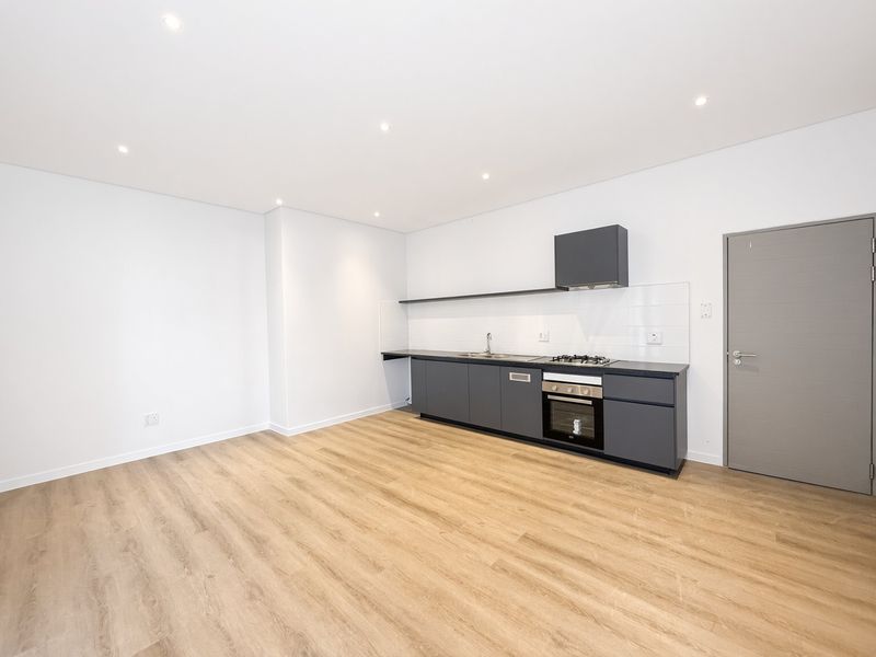 Modern open-plan kitchen featuring dark grey cabinetry, gas hob, electric oven, and light wood-look laminate flooring in a clean, minimalist space.