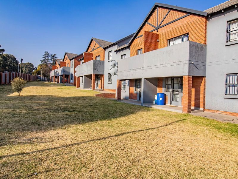Rear view of a multi-unit apartment complex featuring brick and plaster facades, private balconies, and a shared communal garden area.
