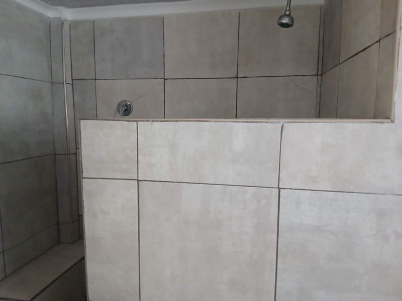 A functional shower area featuring neutral wall tiles, a built-in shower bench, and standard chrome shower fixtures.
