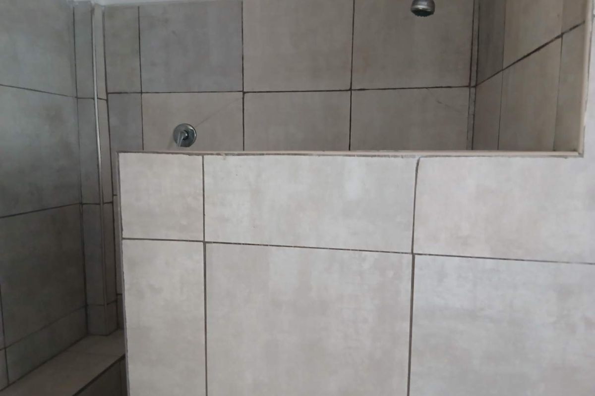 A functional shower area featuring neutral wall tiles, a built-in shower bench, and standard chrome shower fixtures.