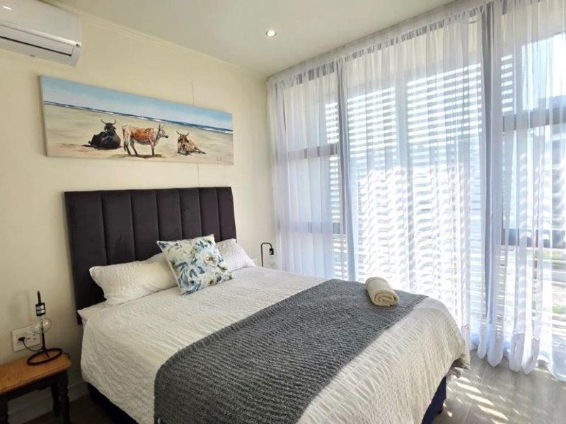 A bright and modern bedroom featuring large floor-to-ceiling windows, tiled flooring, and a wall-mounted split-system air conditioner.