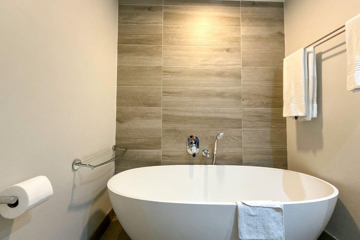 Modern bathroom featuring a sleek freestanding bathtub, wall-mounted chrome fixtures, and stylish wood-look tiled feature wall.