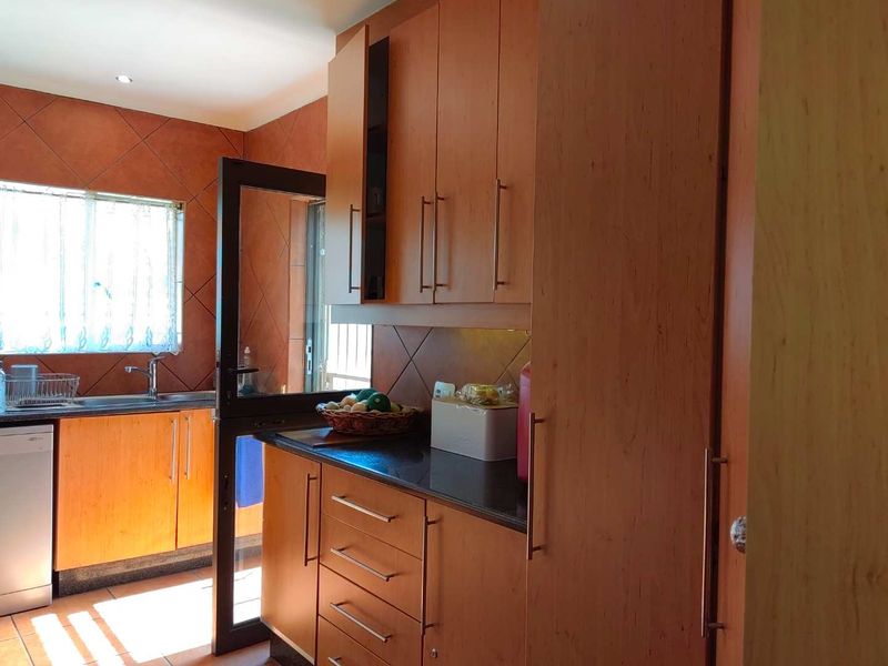 A functional kitchen featuring wood-finish cabinetry, dark countertops, a stainless steel sink, and tiled wall finishes with direct access to the exterior.