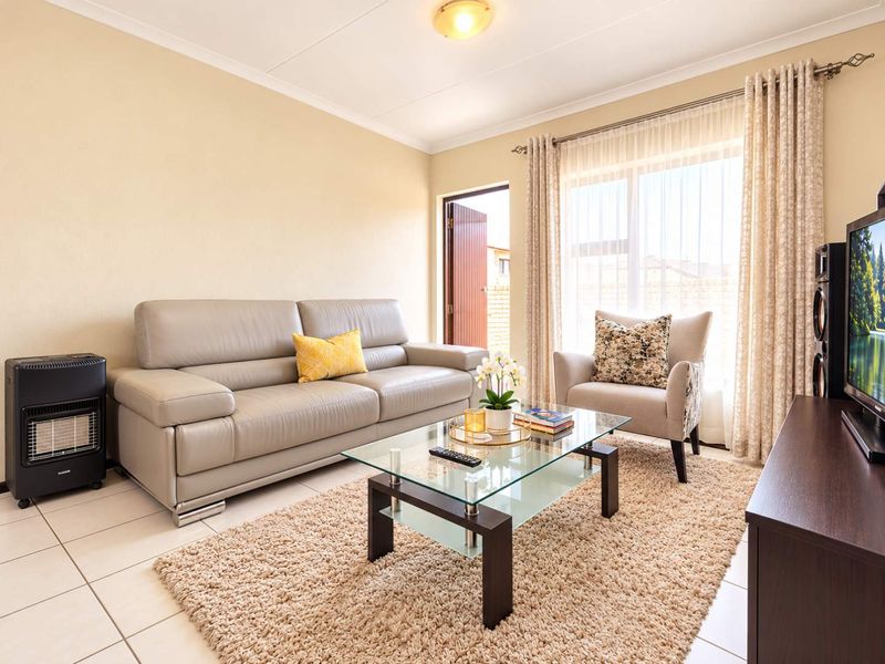 A well-maintained living room featuring tiled flooring, neutral walls, and a sliding glass door providing natural light and access to the exterior.