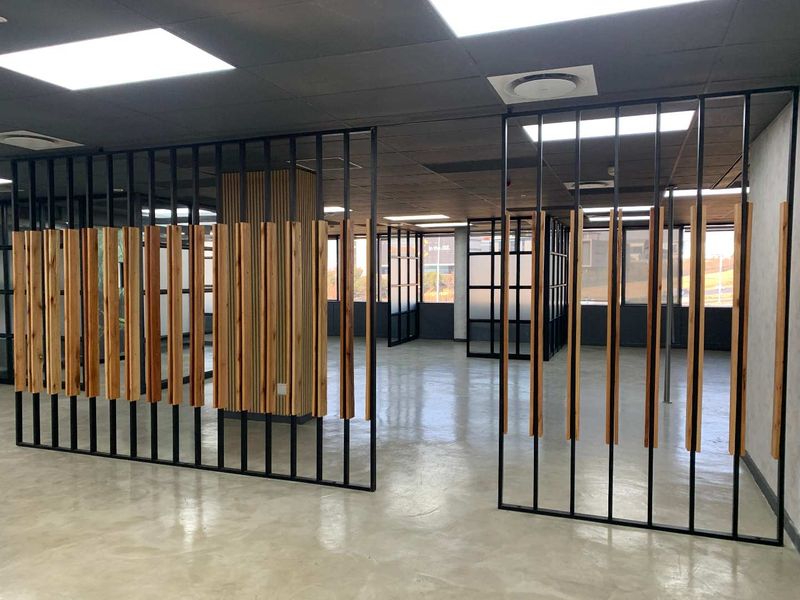 Modern open-plan office space featuring polished concrete floors, contemporary timber slat dividers, black metal partitions, and recessed ceiling lighting.