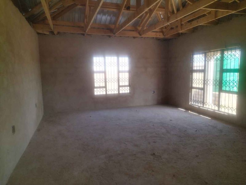 An unfinished interior space featuring exposed timber roof trusses, plastered masonry walls, and security burglar bars on the windows.