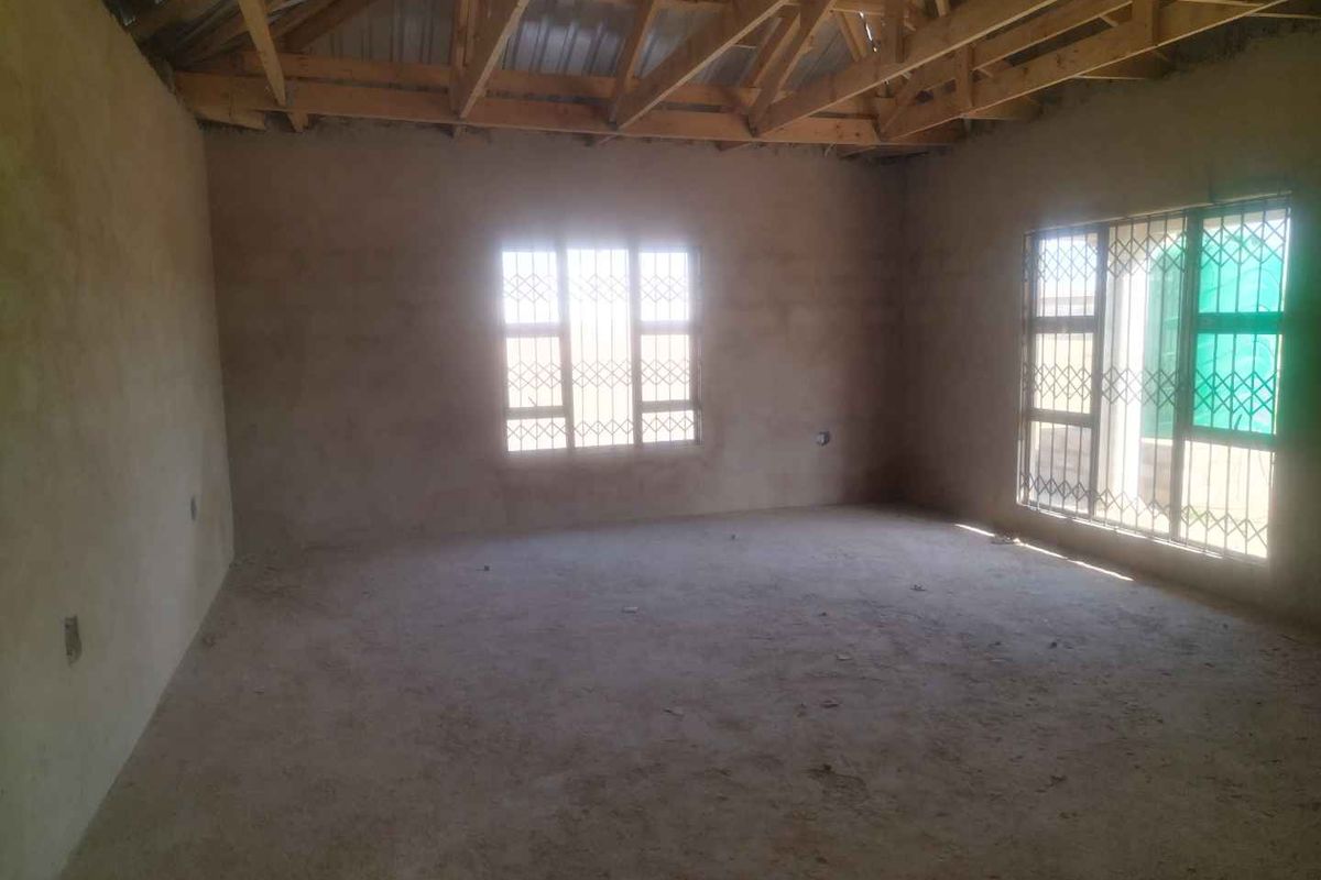 An unfinished interior space featuring exposed timber roof trusses, plastered masonry walls, and security burglar bars on the windows.