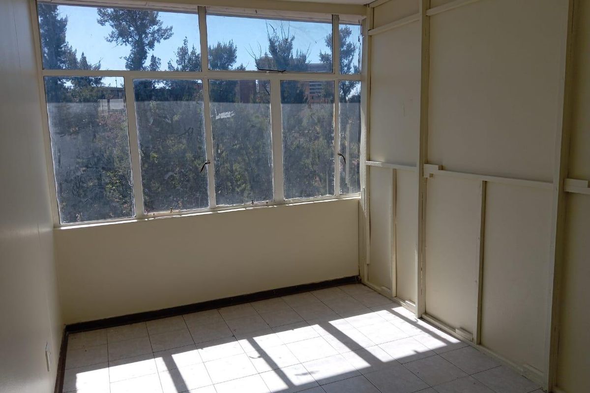An empty bedroom featuring large windows with natural light, tiled flooring, and unfinished wall paneling, offering a blank canvas for renovation.