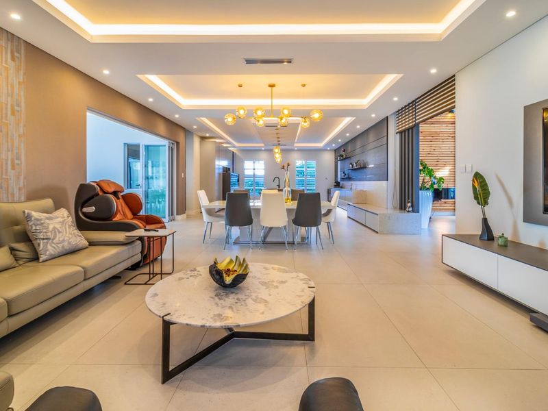 Spacious open-plan living and dining area featuring modern tray ceilings with recessed lighting, large format floor tiles, and seamless flow to outdoor spaces.
