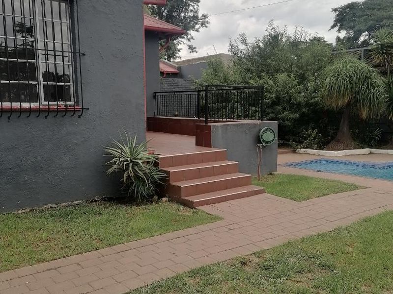 Rear exterior view featuring a tiled patio, paved walkway, and a swimming pool set within a landscaped garden area.