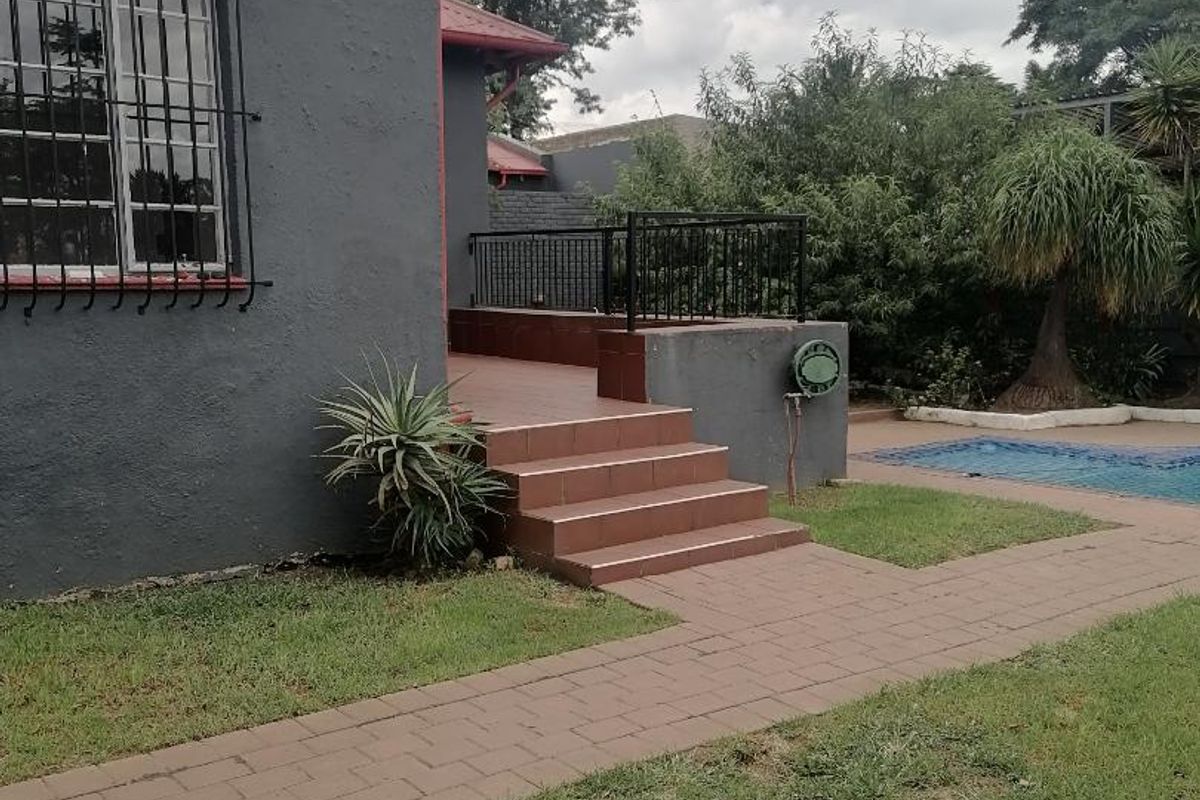 Rear exterior view featuring a tiled patio, paved walkway, and a swimming pool set within a landscaped garden area.