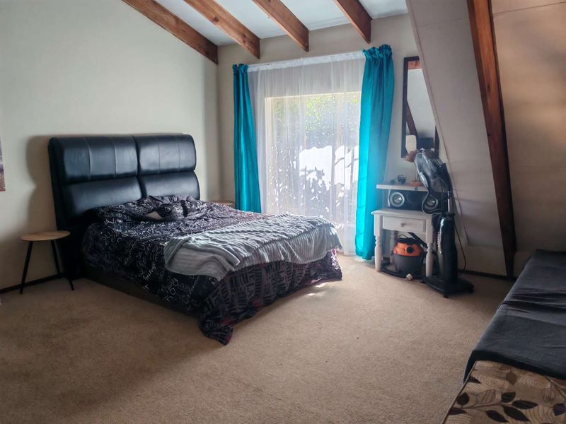 Spacious bedroom featuring exposed timber ceiling beams, carpeted flooring, and a sliding glass door providing natural light.