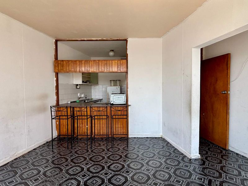 Open plan living area featuring a breakfast bar and a functional kitchen pass-through, offering potential for modernization and cosmetic updates.