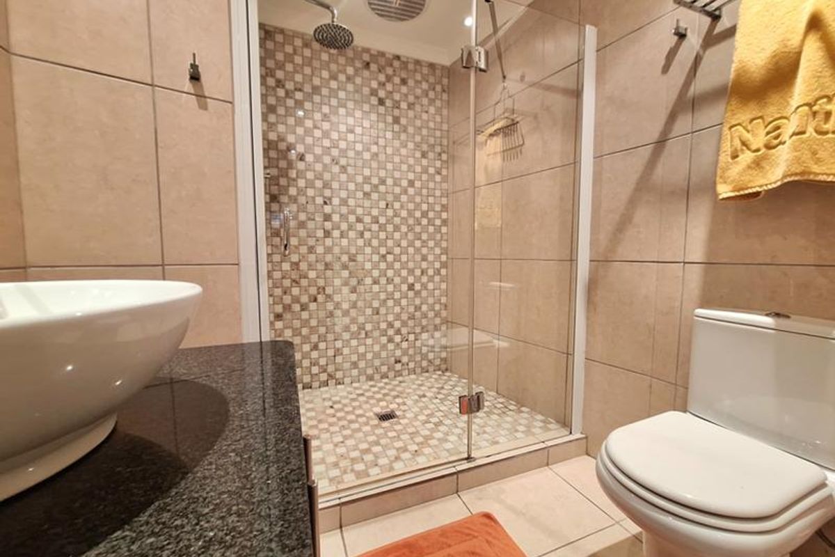 A modern bathroom featuring a glass-enclosed shower with mosaic tile accents, a granite vanity top with a vessel sink, and a standard toilet.