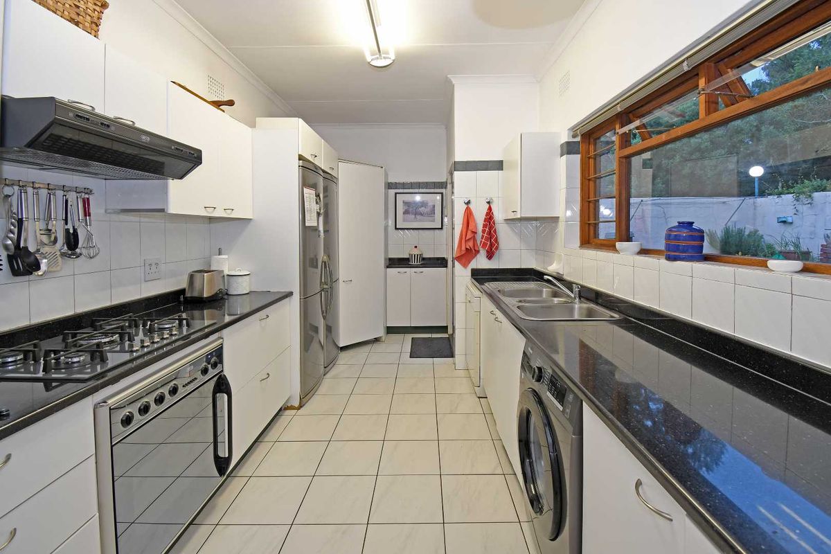A functional galley-style kitchen featuring white cabinetry, dark stone countertops, a gas cooktop, and integrated laundry facilities with tiled flooring.