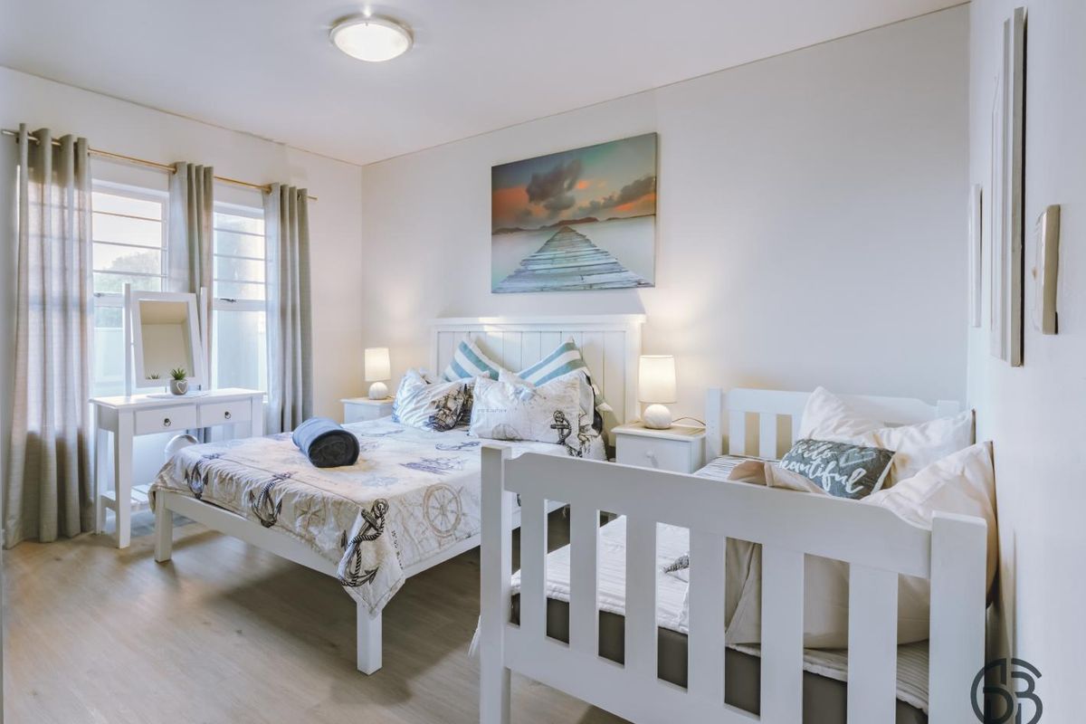 A bright and well-maintained bedroom featuring light wood-look flooring, neutral walls, and large windows that provide ample natural light.