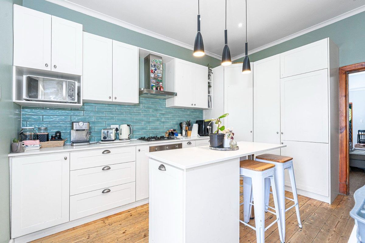 Modern kitchen featuring white cabinetry, a central island, gas cooktop, subway tile backsplash, and warm timber flooring.