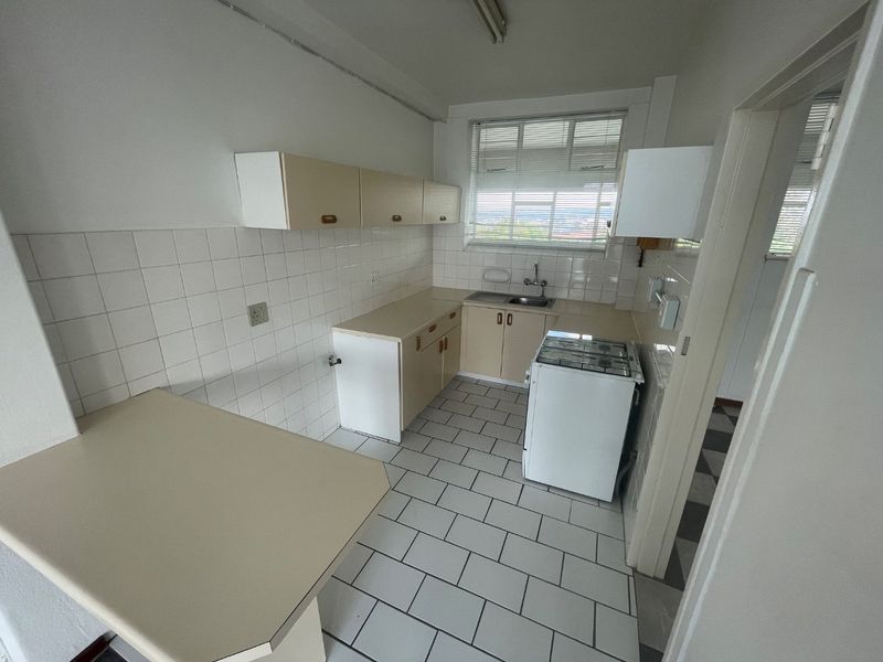 A functional kitchen featuring tiled flooring, white tiled backsplash, built-in cabinetry, and a freestanding stove, offering potential for modern renovation.