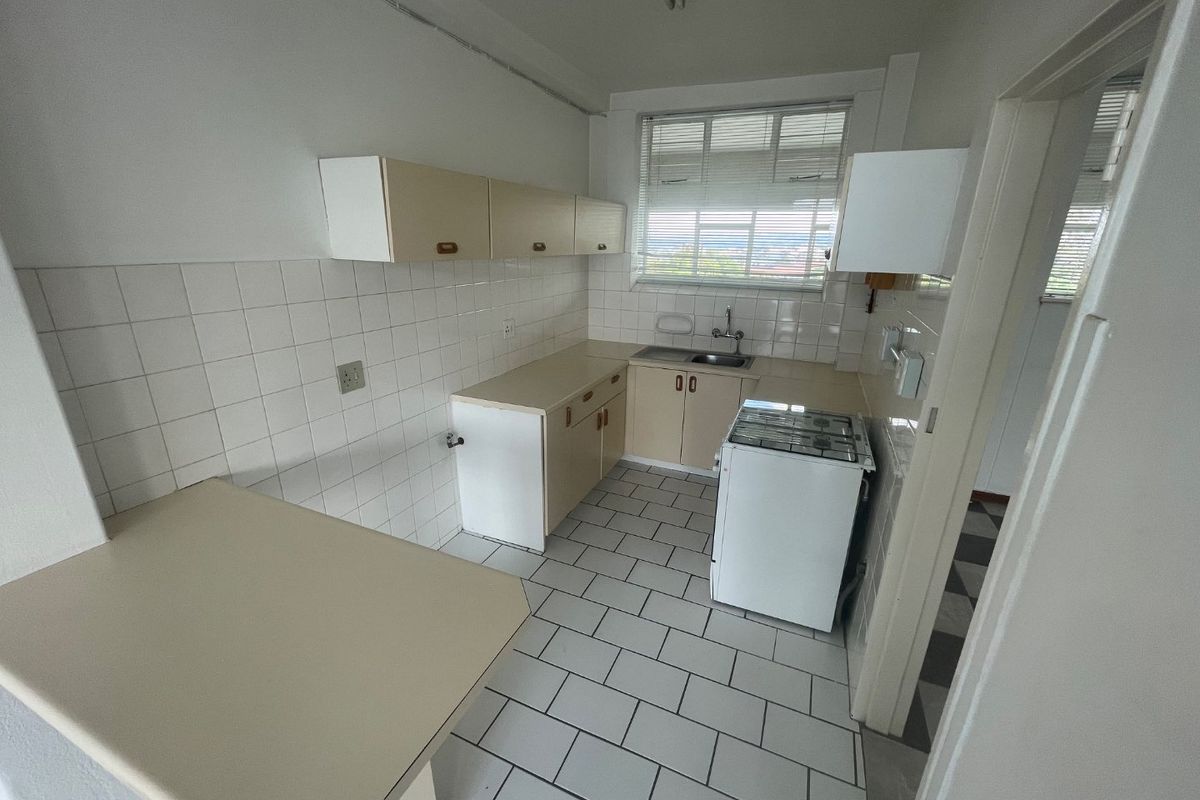 A functional kitchen featuring tiled flooring, white tiled backsplash, built-in cabinetry, and a freestanding stove, offering potential for modern renovation.