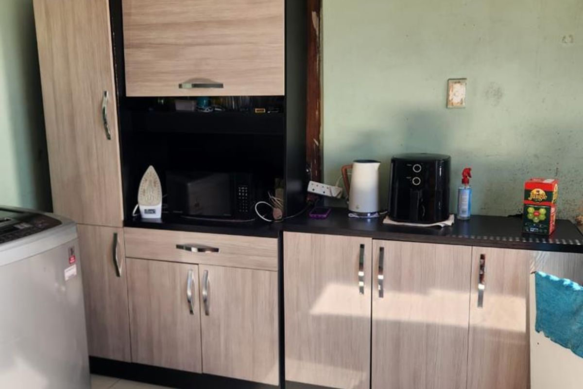 A kitchen area featuring built-in cabinetry and tiled flooring, currently showing signs of wear including wall cracks and damaged ceiling tiles.