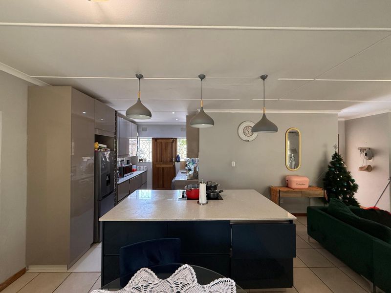 An open-plan living and kitchen area featuring a central island with a hob, modern cabinetry, and tiled flooring throughout.