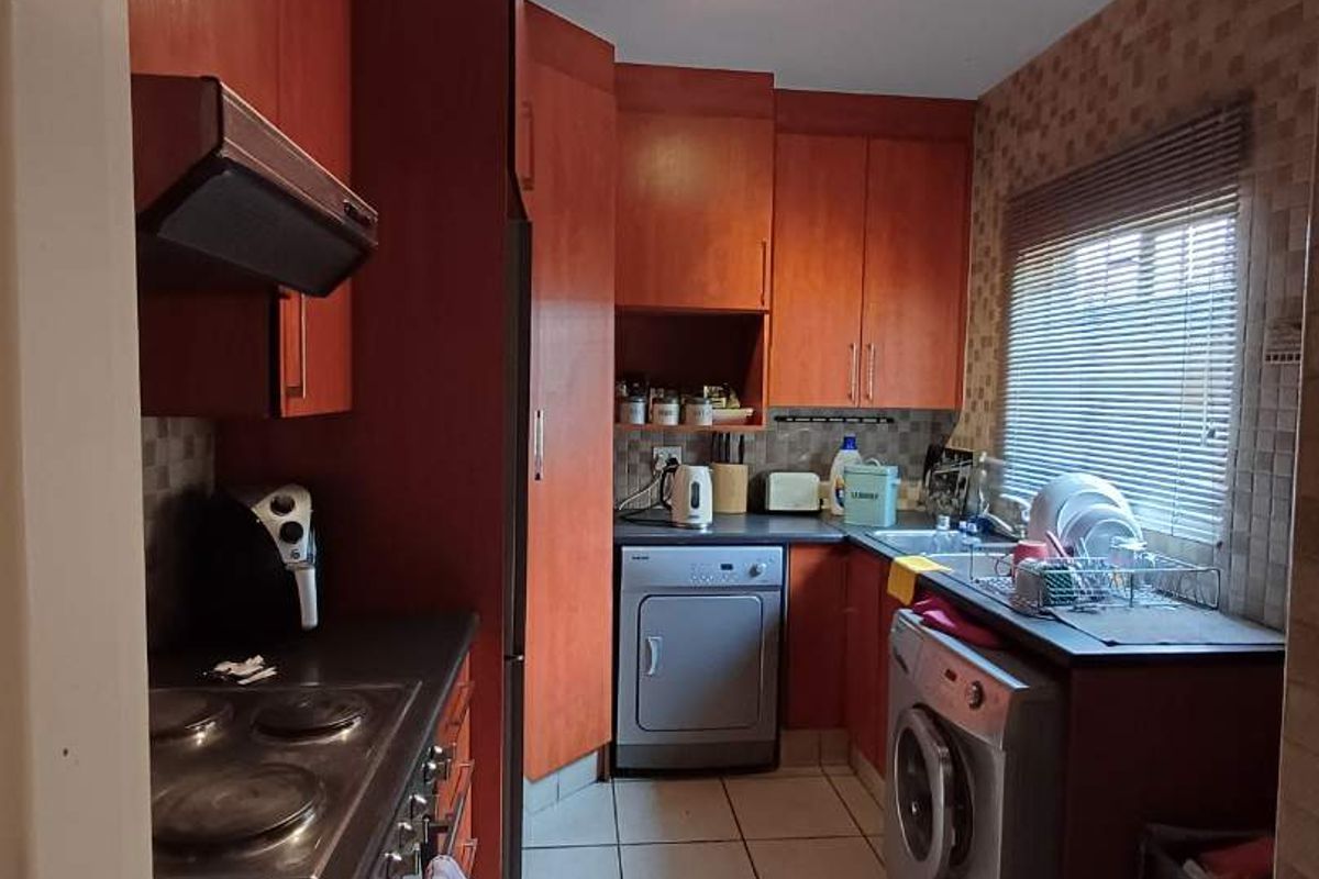 A functional kitchen featuring wood-toned cabinetry, integrated hob and extractor fan, tiled flooring, and a dedicated space for laundry appliances.