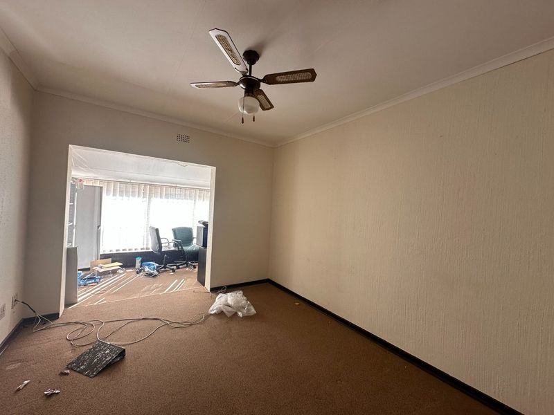 An empty living room featuring a ceiling fan and carpeted flooring, leading into an adjacent sunroom area.