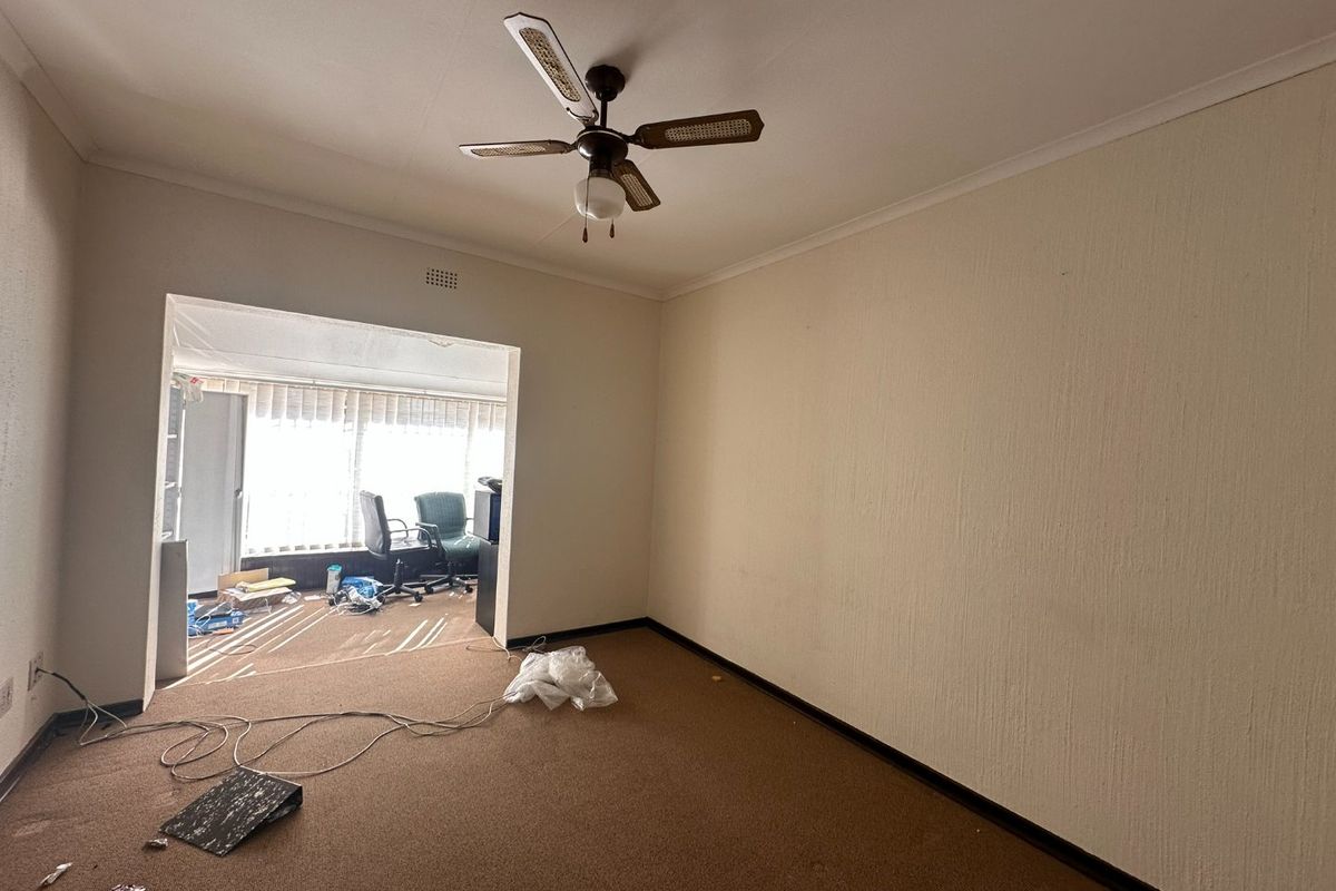 An empty living room featuring a ceiling fan and carpeted flooring, leading into an adjacent sunroom area.
