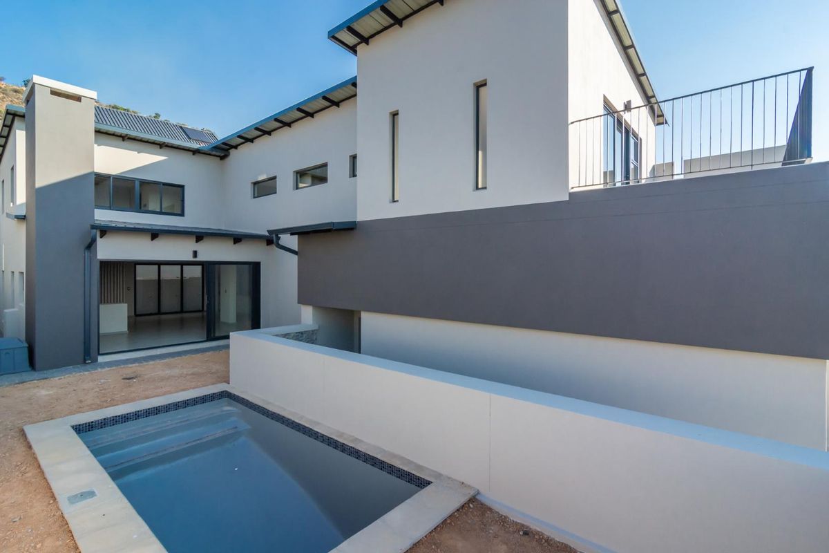 Rear view of a modern two-story house featuring a swimming pool, a balcony, and large sliding glass doors leading into the living area.